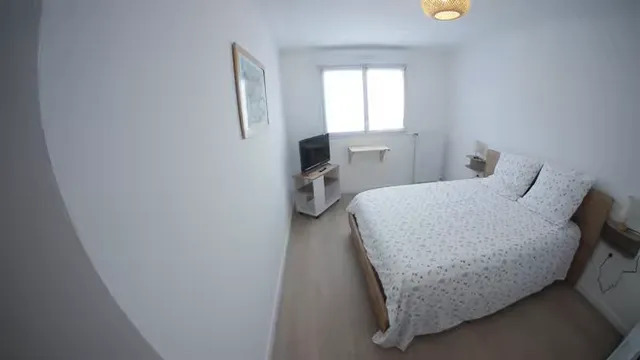 Chambre lumineuse avec lit double, télévision, fenêtre et tables de chevet