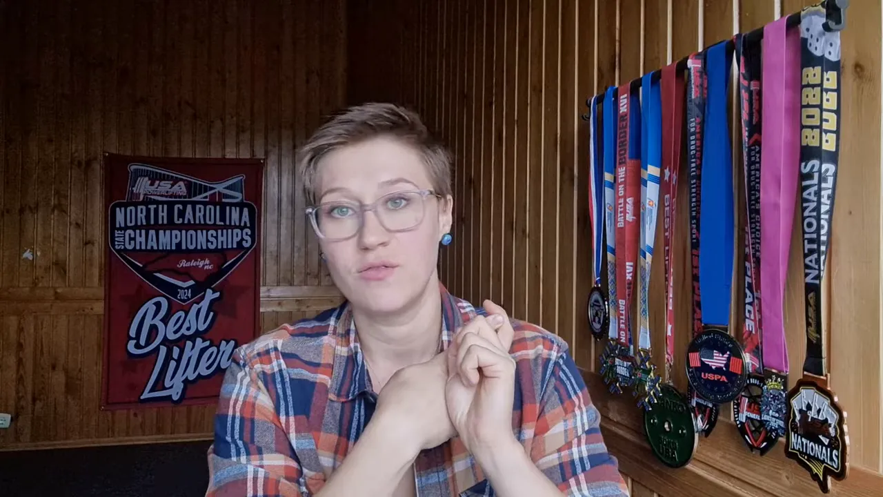 Presenter directly addressing the camera in a wood‑panel room with medals visible — clear, well framed head‑and‑shoulders shot.