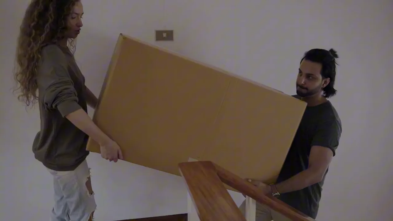 Two people carrying a large cardboard box up a flight of stairs, demonstrating manual/unplanned lifting.