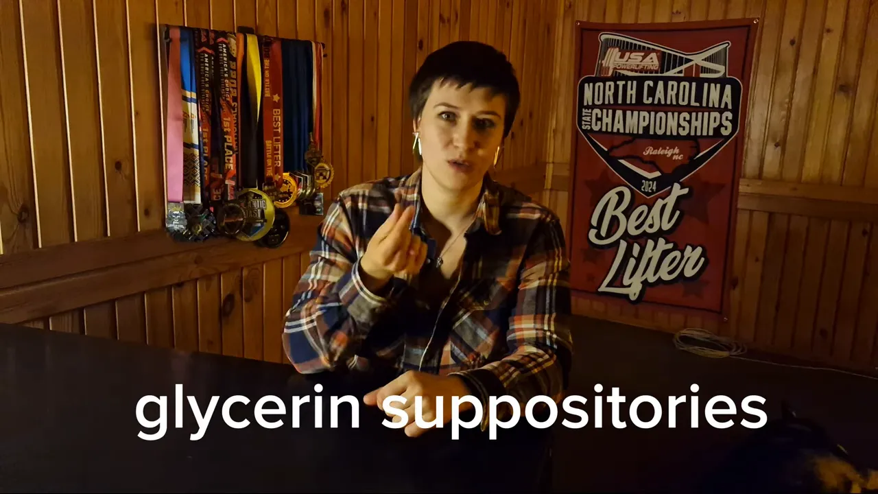 Speaker centered at a table gesturing while describing glycerin suppositories; large on-screen text 'glycerin suppositories' across the bottom with medals and 'Best Lifter' banner behind.
