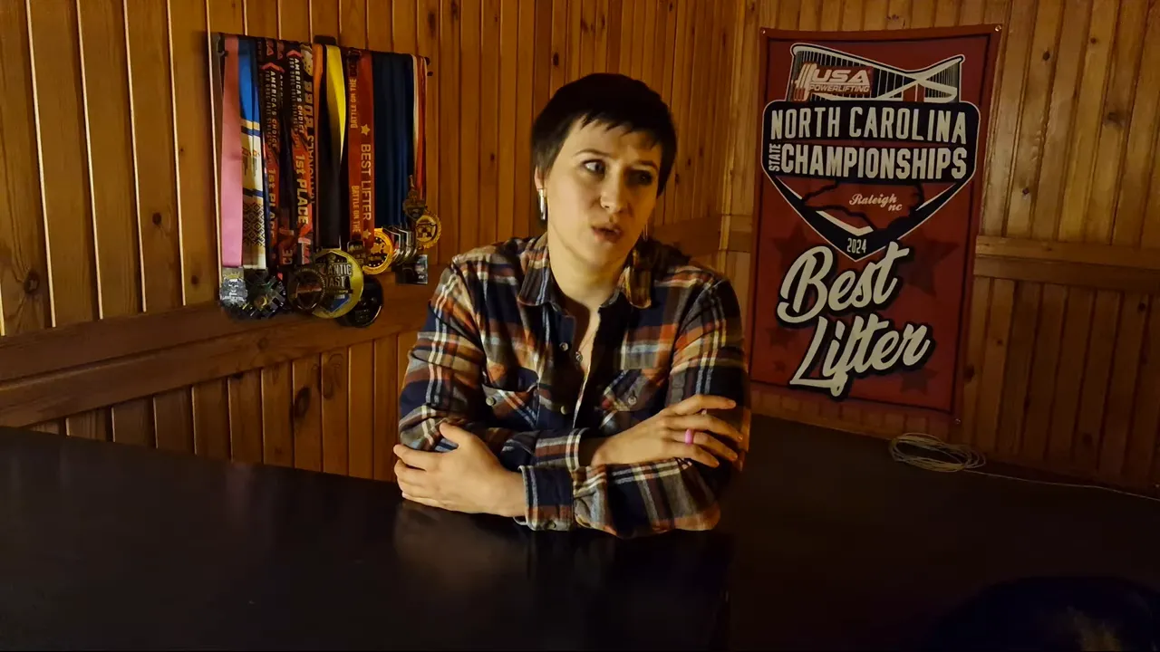Woman explaining the significance of green amniotic fluid and meconium during labor, seated with medals and a 'Best Lifter' sign behind her.