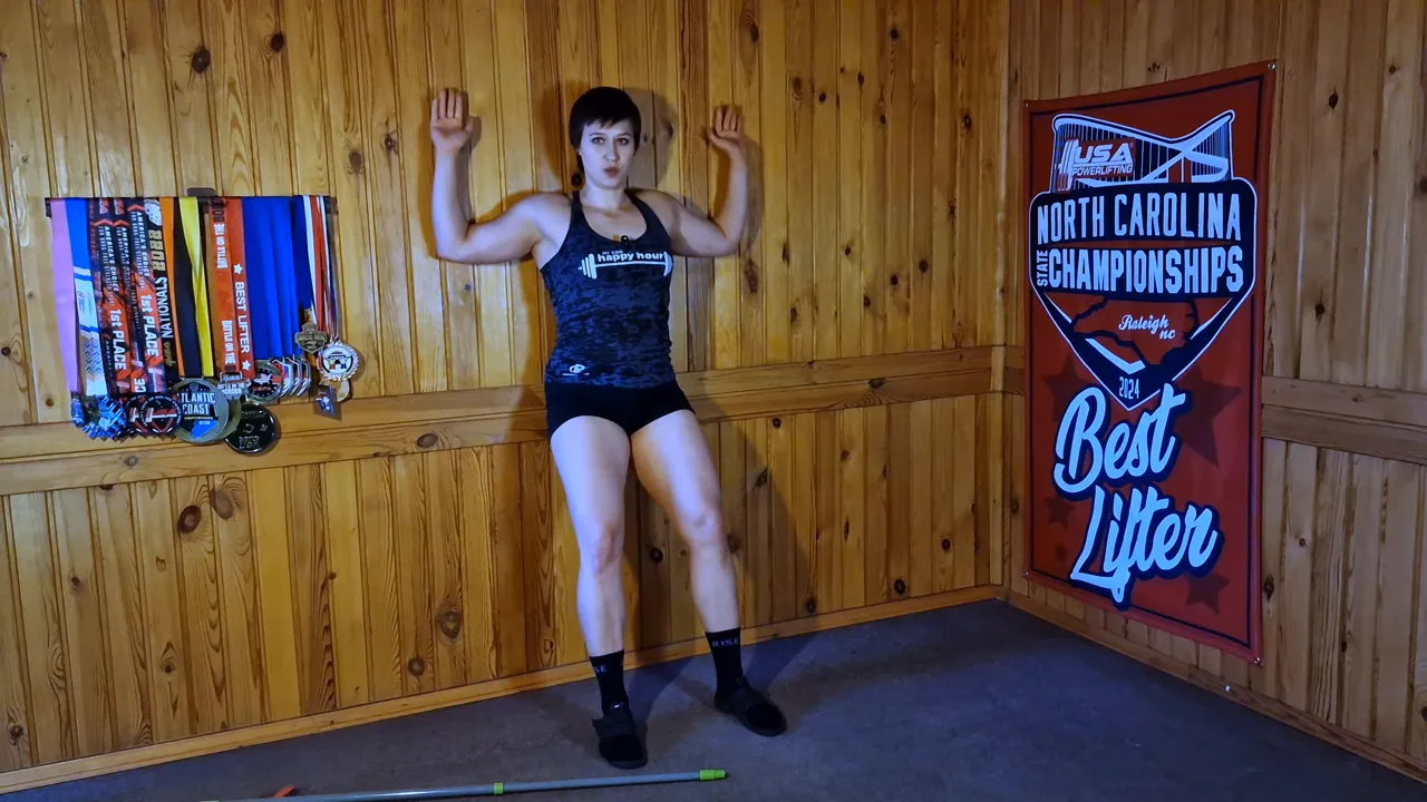 Full-body shot of athlete doing elbow wall slides against a wood-paneled wall demonstrating thoracic mobility