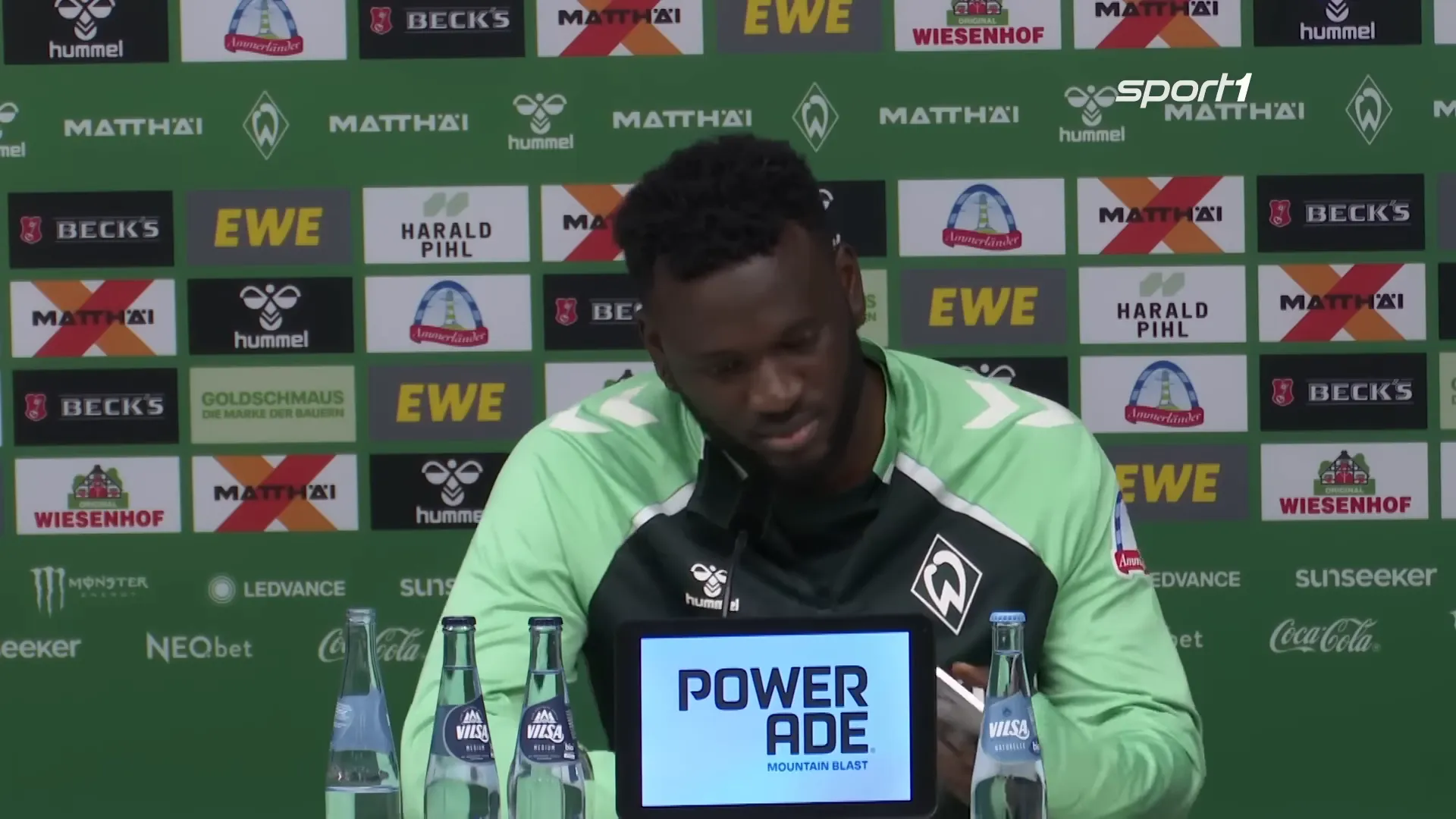 Boniface scrollt während der Pressekonferenz auf seinem Handy