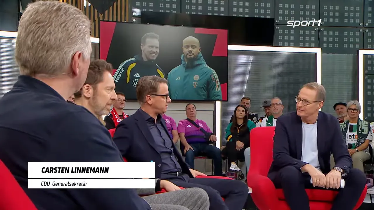 Diskussionsrunde im Studio mit großem Bildschirm, der zwei Trainer-Porträts zeigt