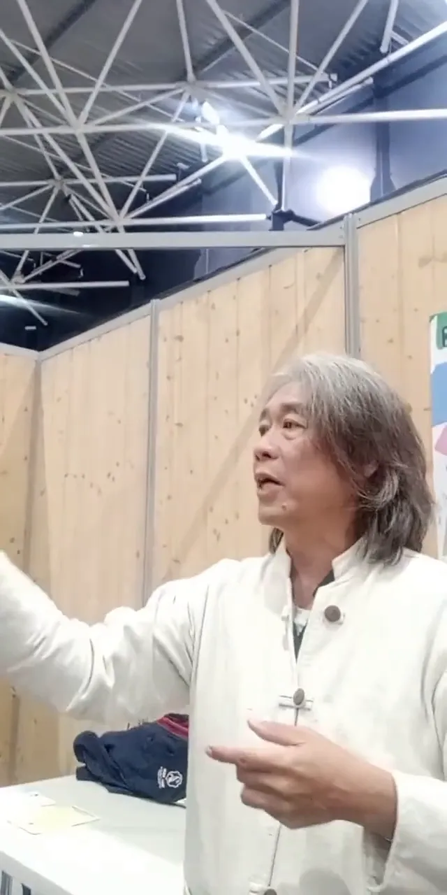 Intervenant en veste claire faisant un geste didactique avec les mains, posture ouverte.