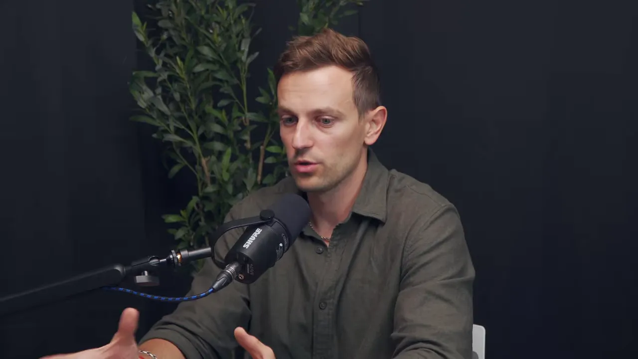 Мужчина в студии жестами подчёркивает мысль во время интервью, кадр по пояс с видимыми руками и микрофоном.