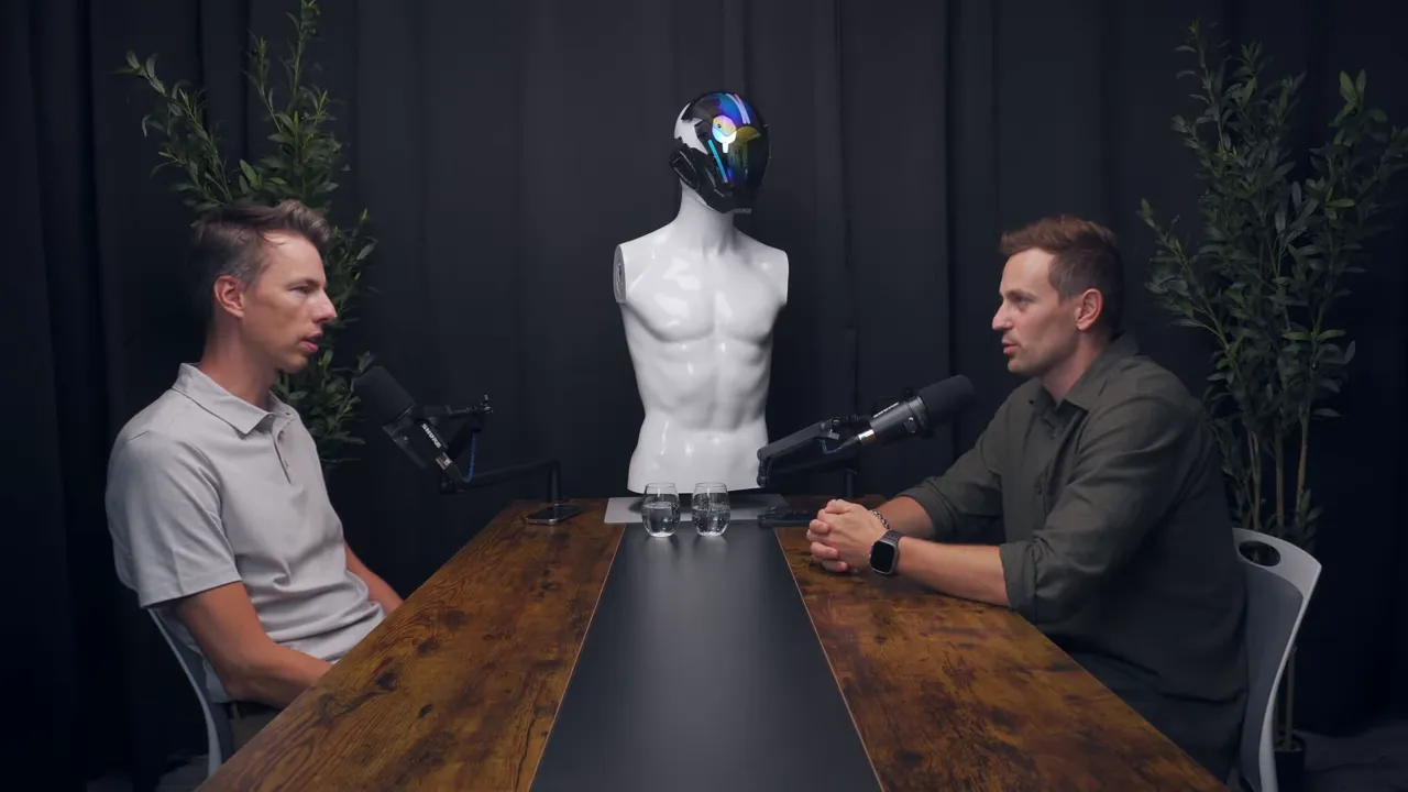 Широкий план: два собеседника сидят напротив друг друга за столом в студии, в центре манекен и микрофоны.