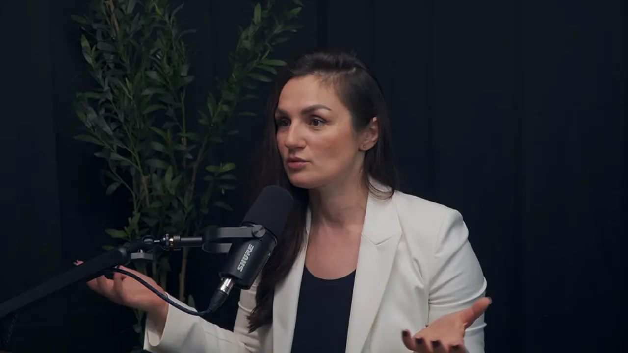 Марина Морган в белом пиджаке, средний план, активно жестикулирует у микрофона, демонстрируя объяснение ключевых проблем фаундеров.