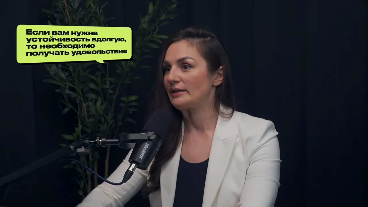 Марина Морган у микрофона с надписью «Если вам нужна устойчивость вдолго, то необходимо получать удовольствие», средний план, чёткое изображение.