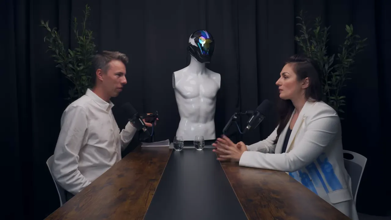 Широкий план: двое ведущих за столом и манекен-робот между ними в студии