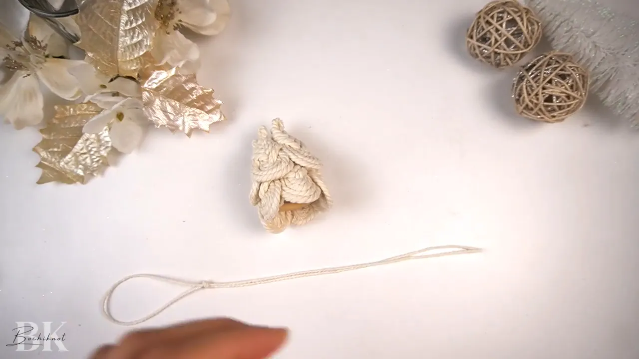 Finished mini macrame tree sitting above a laid-out loop of thin string on a white work surface.