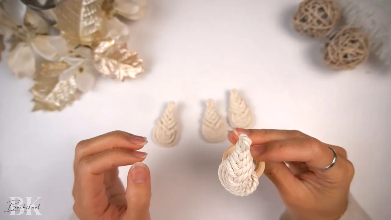 Hands placing a Pipa knot onto a wooden ring to form the ornament's bottom row.