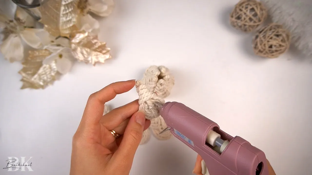 Close-up of hands applying hot glue to the base of a macrame Pipa knot