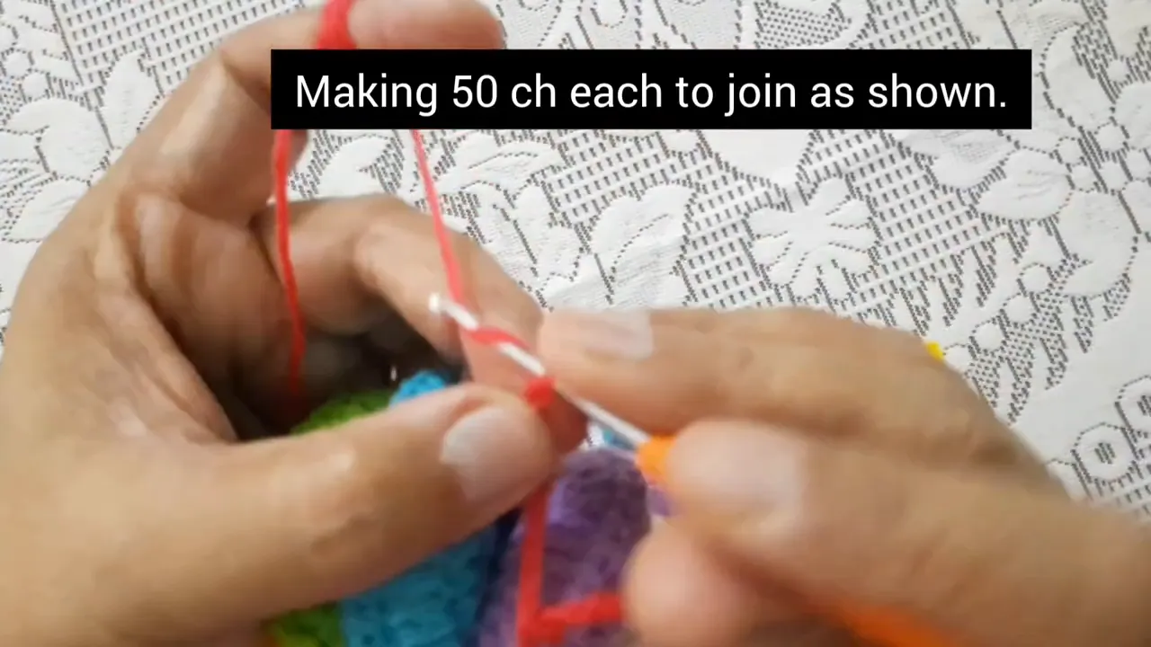 Hands crocheting a red chain beside a multicolored rounded motif assembly with text specifying 50 chains
