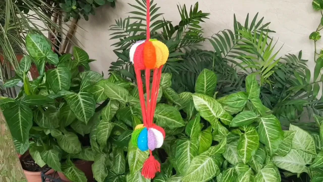 Completed multicolored crochet wind spinner hanging among green plants with red connecting strands and a red tassel