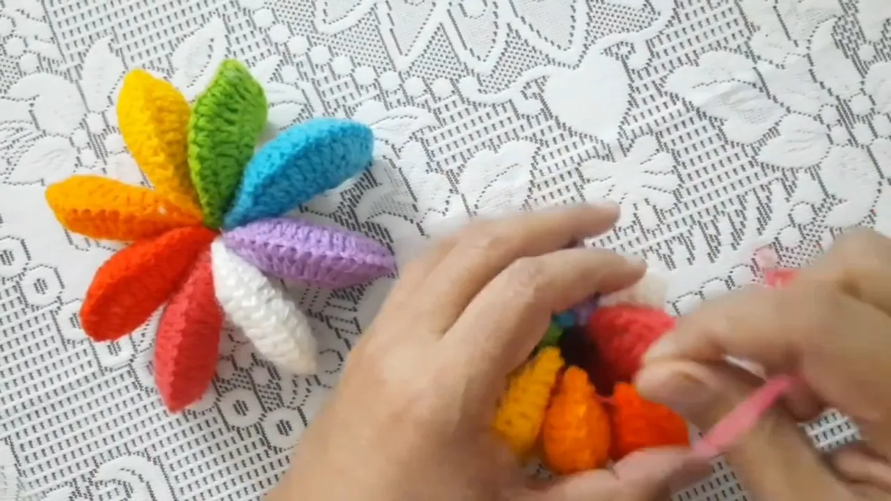 Hands holding a rounded crochet assembly with orange yellow green and turquoise padded sections