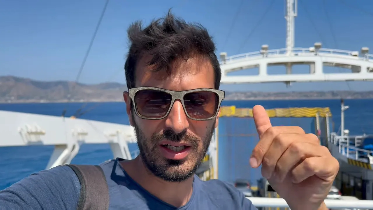 Persona che gesticola sul ponte di un traghetto con lo Stretto di Messina sullo sfondo