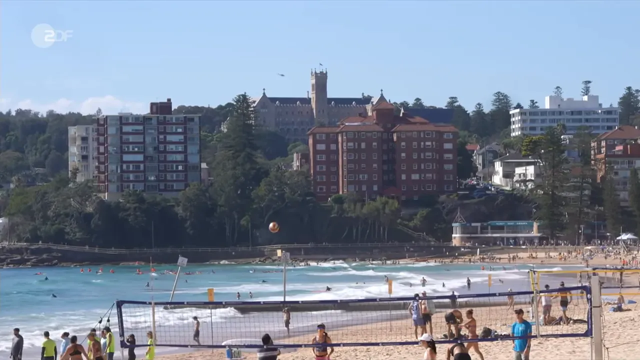 Strandszene in Australien mit Volleyballnetz, Badenden und Bebauung im Hintergrund