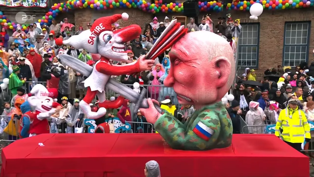 Großer Karnevalswagen mit Narrenfigur 'SATIRE', die auf eine rote Büste einschlägt; viele Zuschauer im Hintergrund