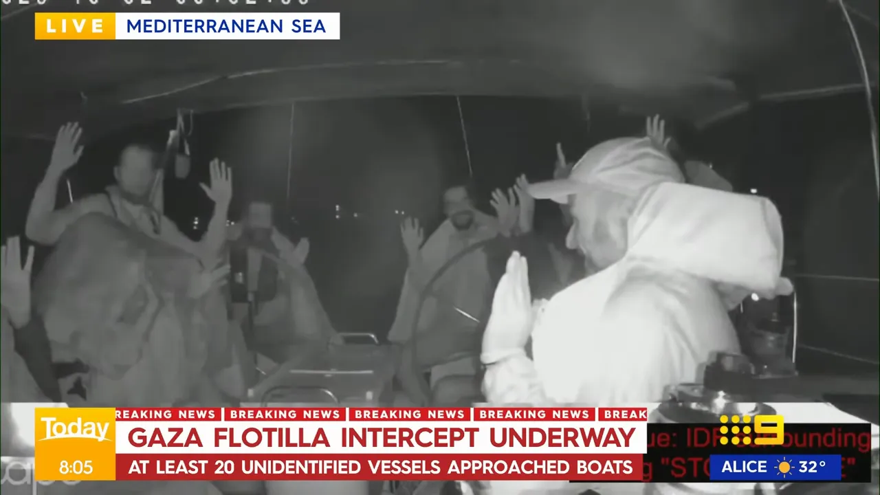 People on deck with hands raised as Israeli forces board or approach