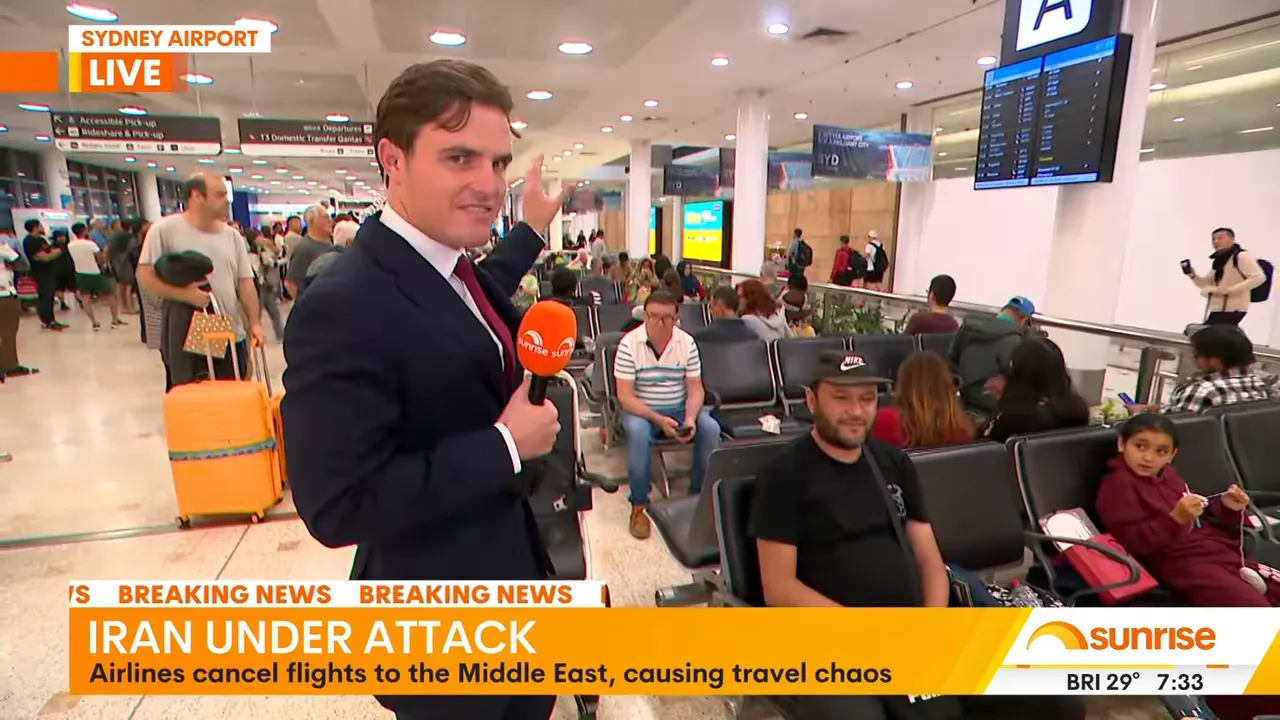 Reporter gesturing to seated passengers and luggage in a busy Sydney Airport terminal