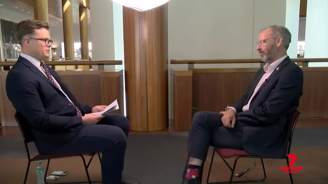 Full-frame wide shot of an interviewer and interviewee seated opposite each other in a formal indoor setting, providing context for a policy discussion; 7 News logo visible.