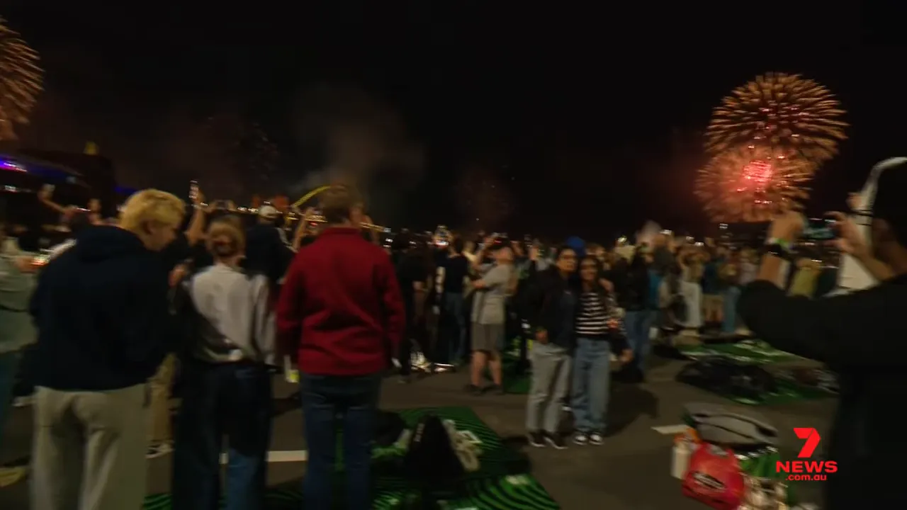 Crowd watching red fireworks burst over Sydney Harbour at night