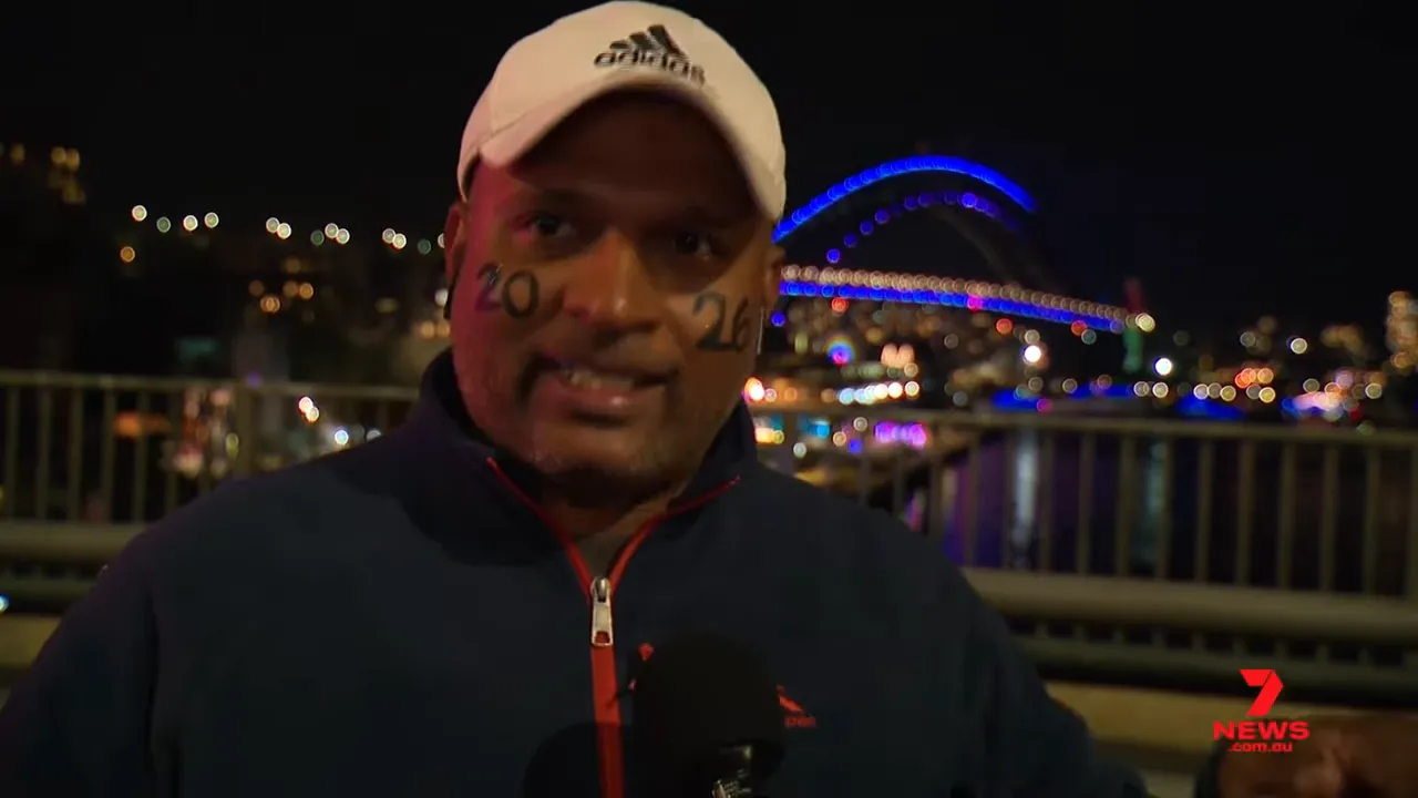 Interviewee with '20' and '26' face paint speaking to camera with the lit Sydney Harbour Bridge behind him
