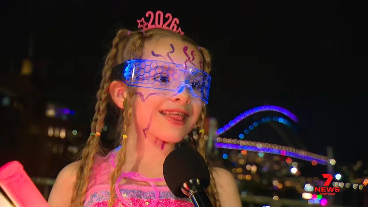 Child in 2026 headband and glowing glasses with Sydney Harbour Bridge lit in the background at night
