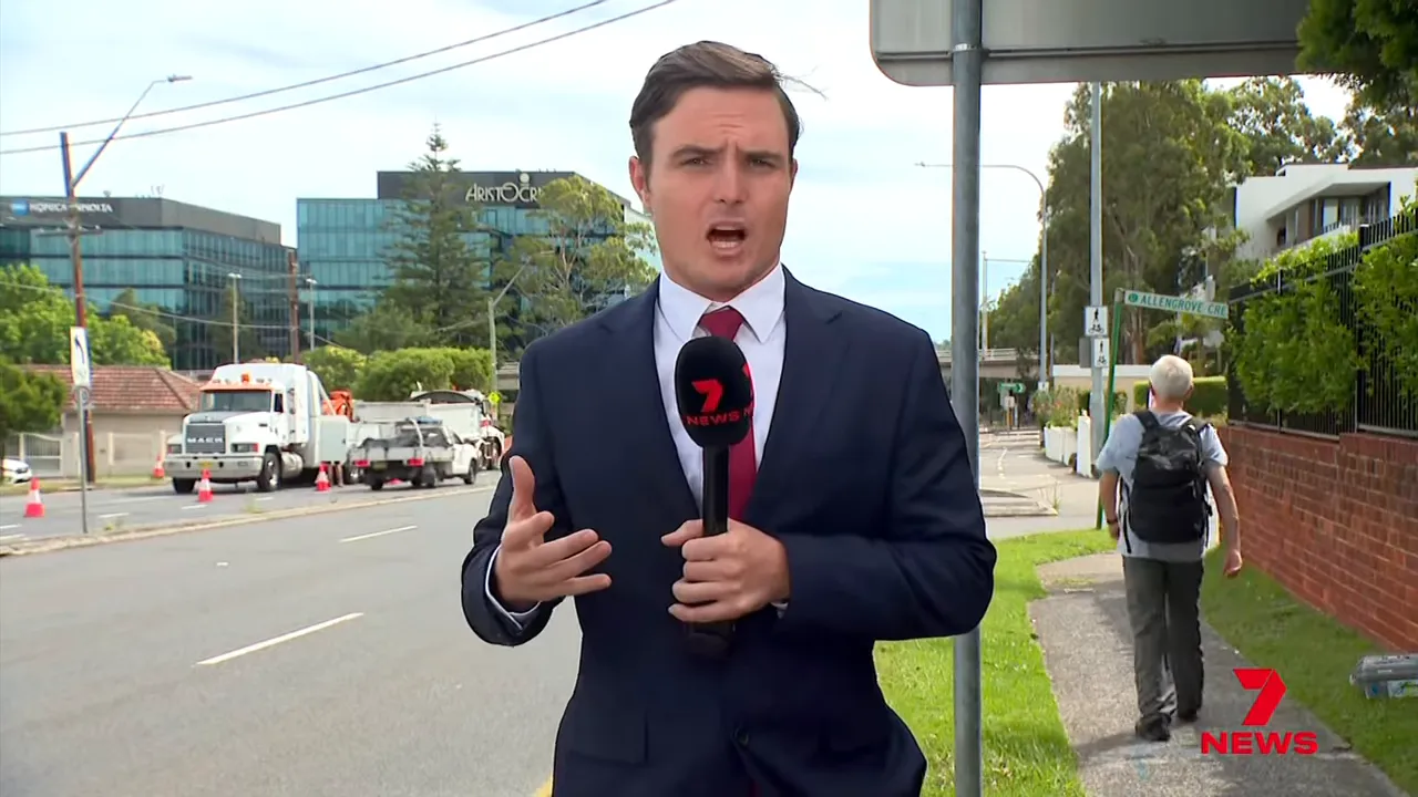 News reporter reporting live on Lane Cove Road with recovery trucks and traffic cones visible behind him, illustrating lane closures