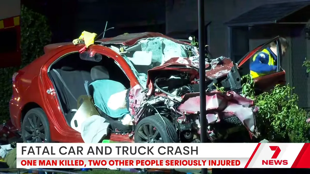 Red Mitsubishi with crushed front and open door at a nighttime crash scene with an emergency worker at the door.