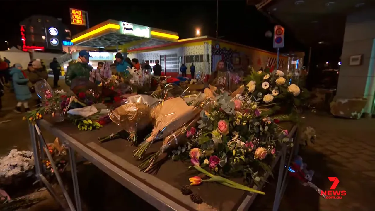 table piled with floral bouquets left as tributes outside the Constellation bar at night