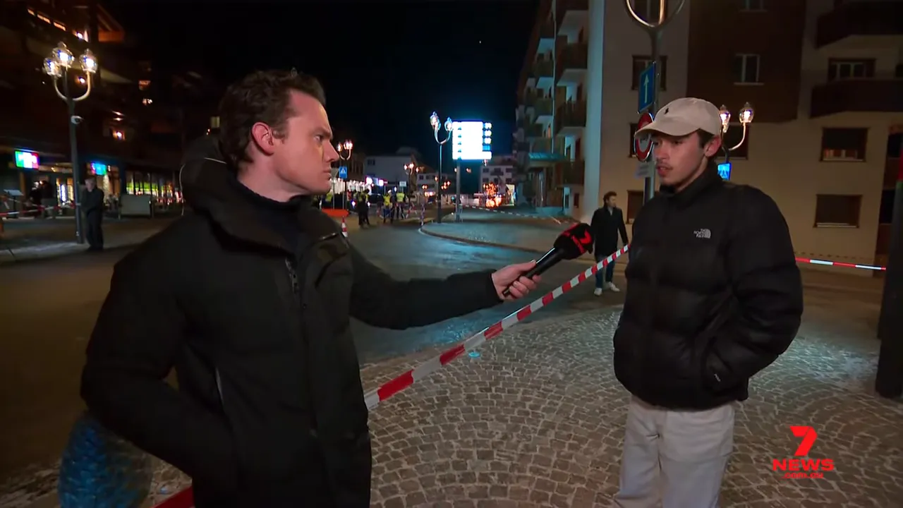 Reporter interviewing a witness in front of cordon tape on a cobbled street at night, emergency activity visible down the road