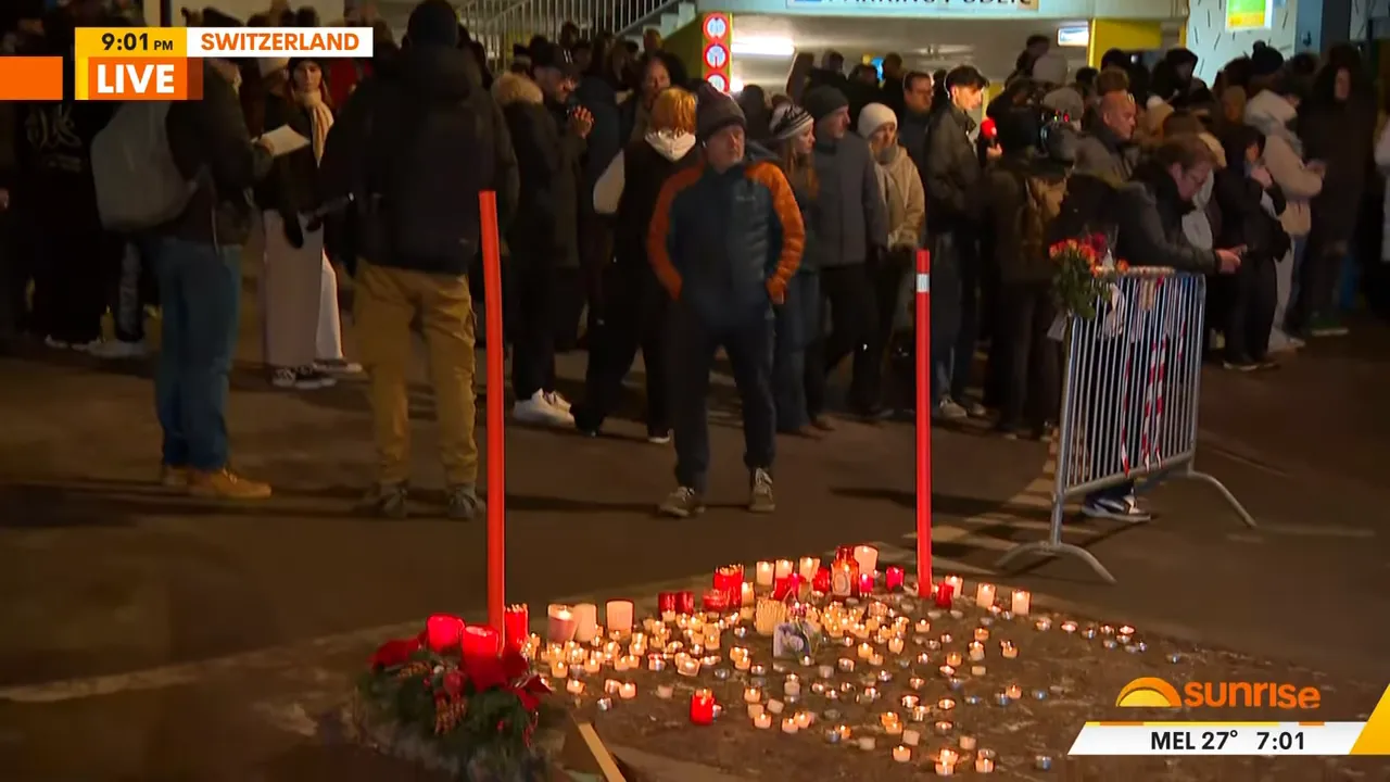 candles and floral tributes on the ground with mourners in background