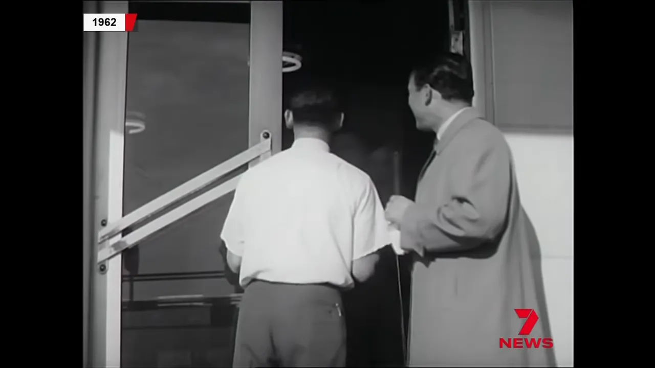 Presenter holding a microphone at a front door while a man enters, black-and-white 1962 footage