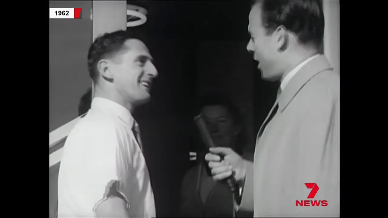 Clear black-and-white 1962 footage of a presenter holding a microphone and a smiling man at his doorstep during a lottery announcement.