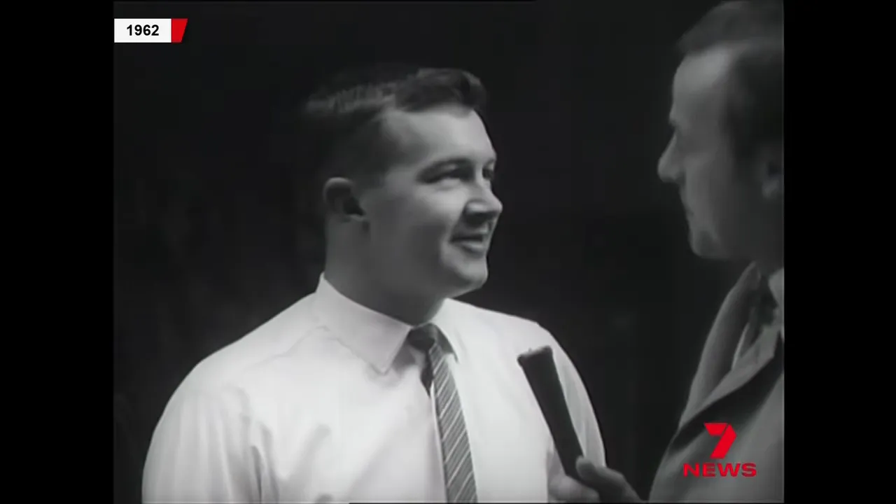 1962 archival still of a smiling lottery syndicate member speaking into a microphone held by the presenter, showing a clear interaction.