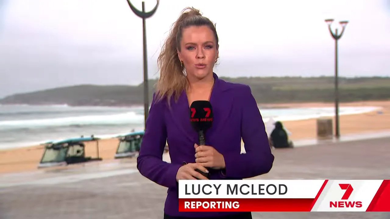 Reporter standing on Maroubra Beach with surf rescue vehicles and rough surf in the background