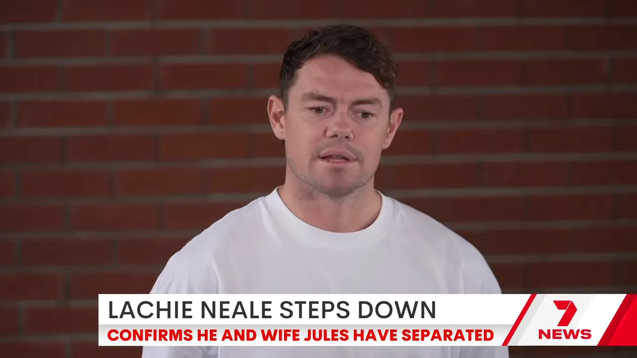 A man in a white shirt speaking in front of a brick wall during a prepared statement, framed by a news chyron at the bottom.