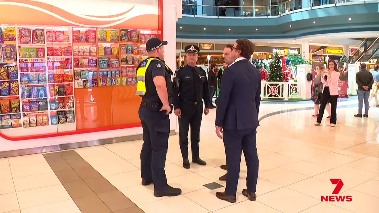 Police officer and uniformed officers speaking with officials in a busy shopping centre concourse.