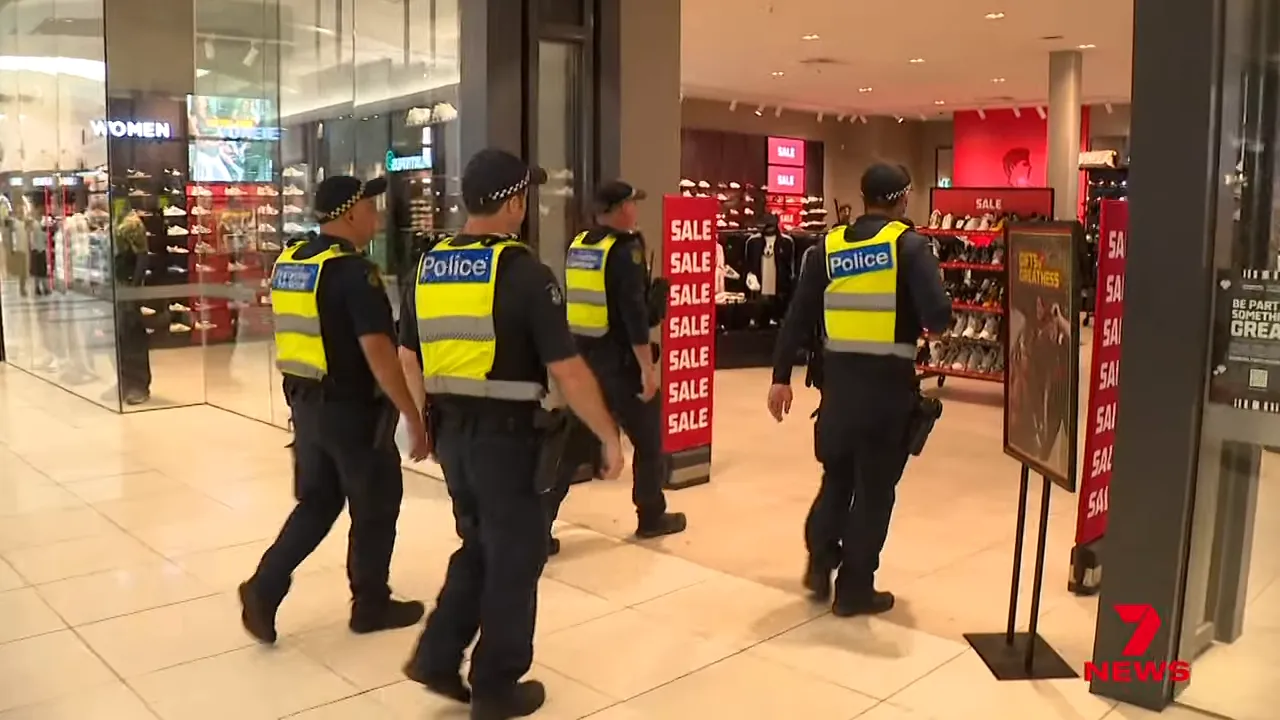 Group of police officers in high-visibility vests walking into a retail store inside a shopping mall.