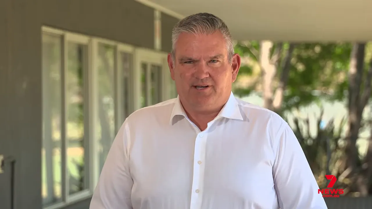 Centered shot of a Major Roads Projects Victoria official in a white shirt speaking outdoors with windows and trees behind him, 7 News watermark