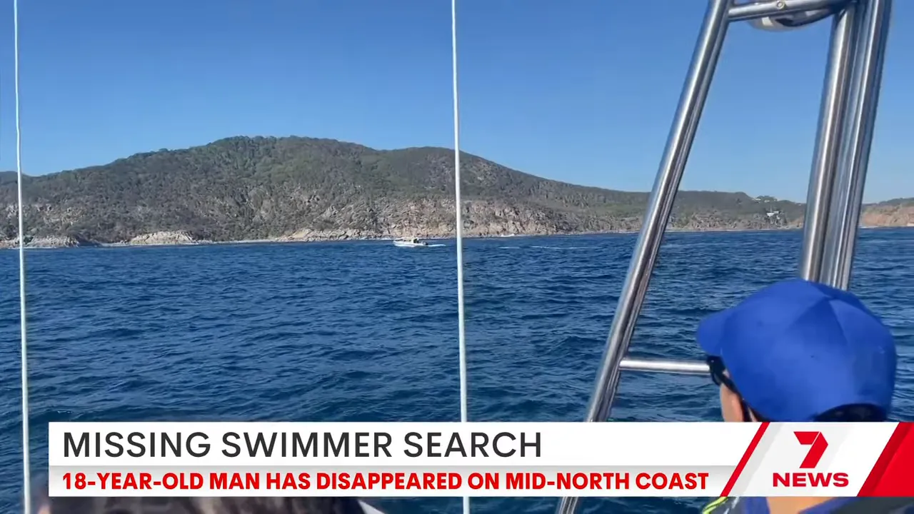 View from a search boat looking toward the rocky coastline at Little Bay, Arakoon, with rescue personnel on deck and choppy sea conditions.