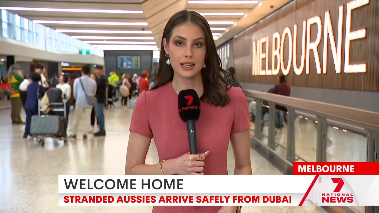 News reporter delivering a live update at Melbourne airport arrivals with the large 'MELBOURNE' sign and passengers in the background