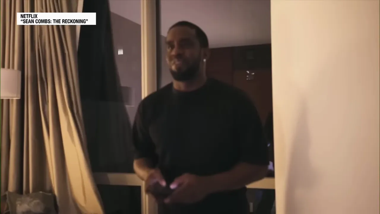 Man standing in a dim hotel room holding a phone near a window with curtains, candid documentary still.