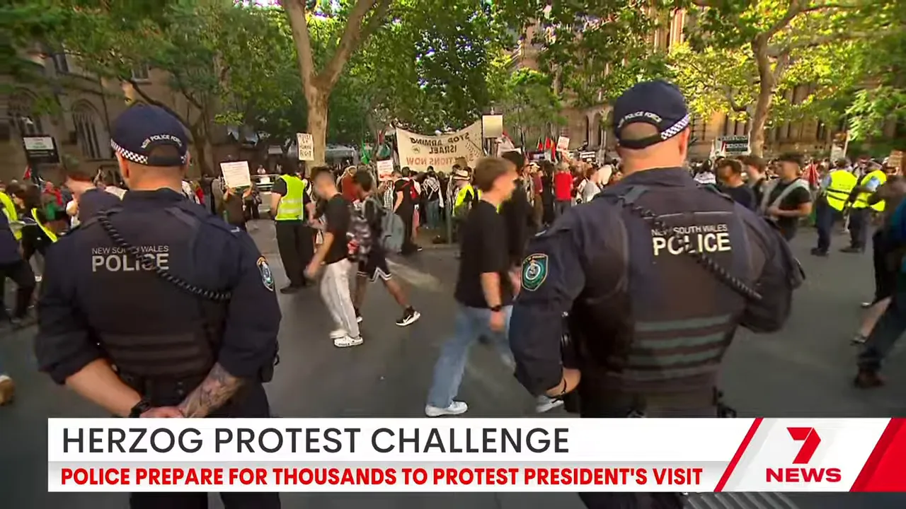 Two New South Wales police officers standing with their backs to camera watching a crowd of protesters and marchers