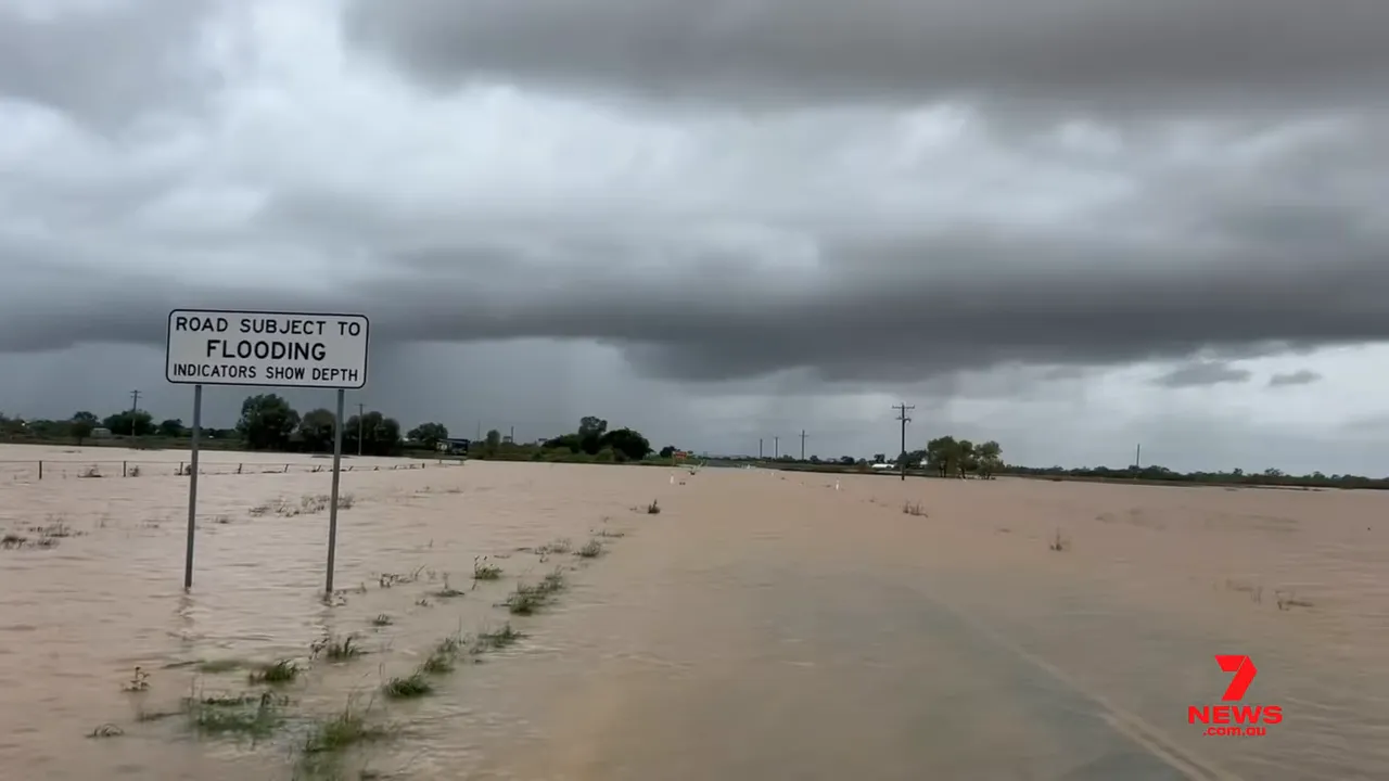 Road subject to flooding sign with surrounding plains submerged under brown floodwater