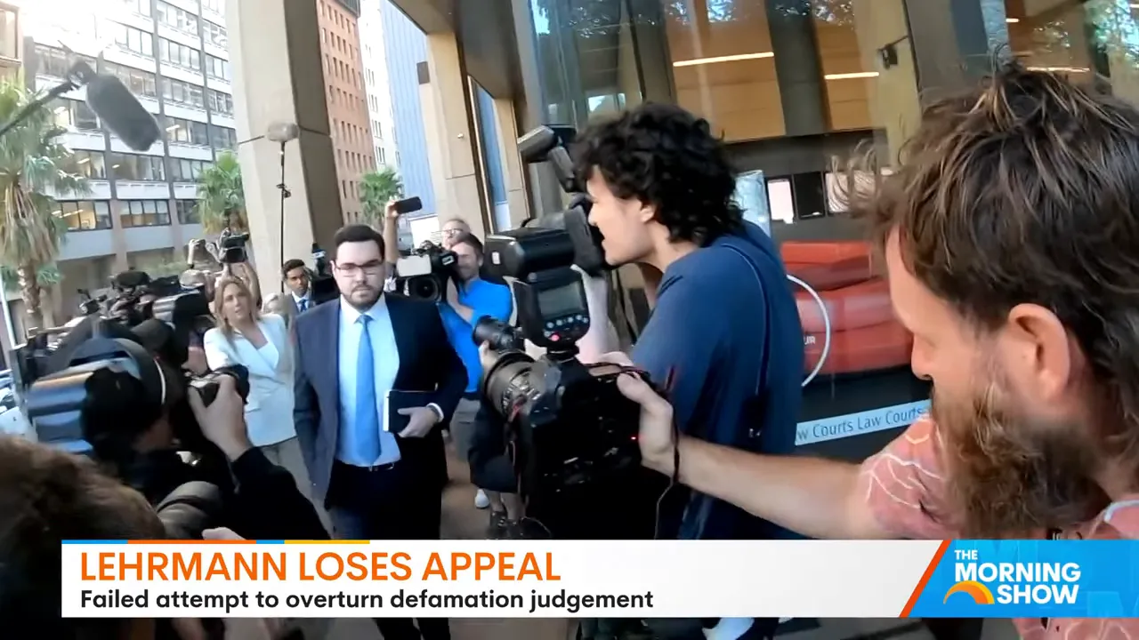 Man in a suit walking through a ring of photographers and cameramen outside a courthouse entrance.
