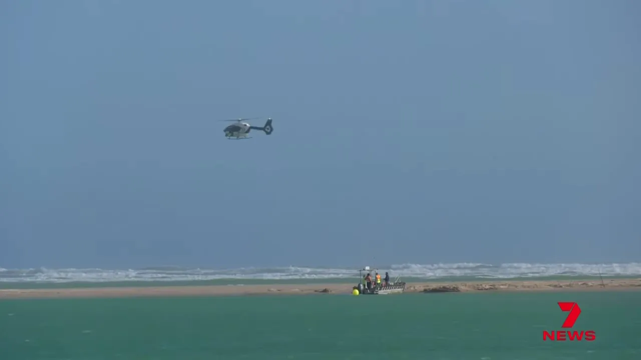 Helicopter hovering over ocean with a recovery boat near a sandbar