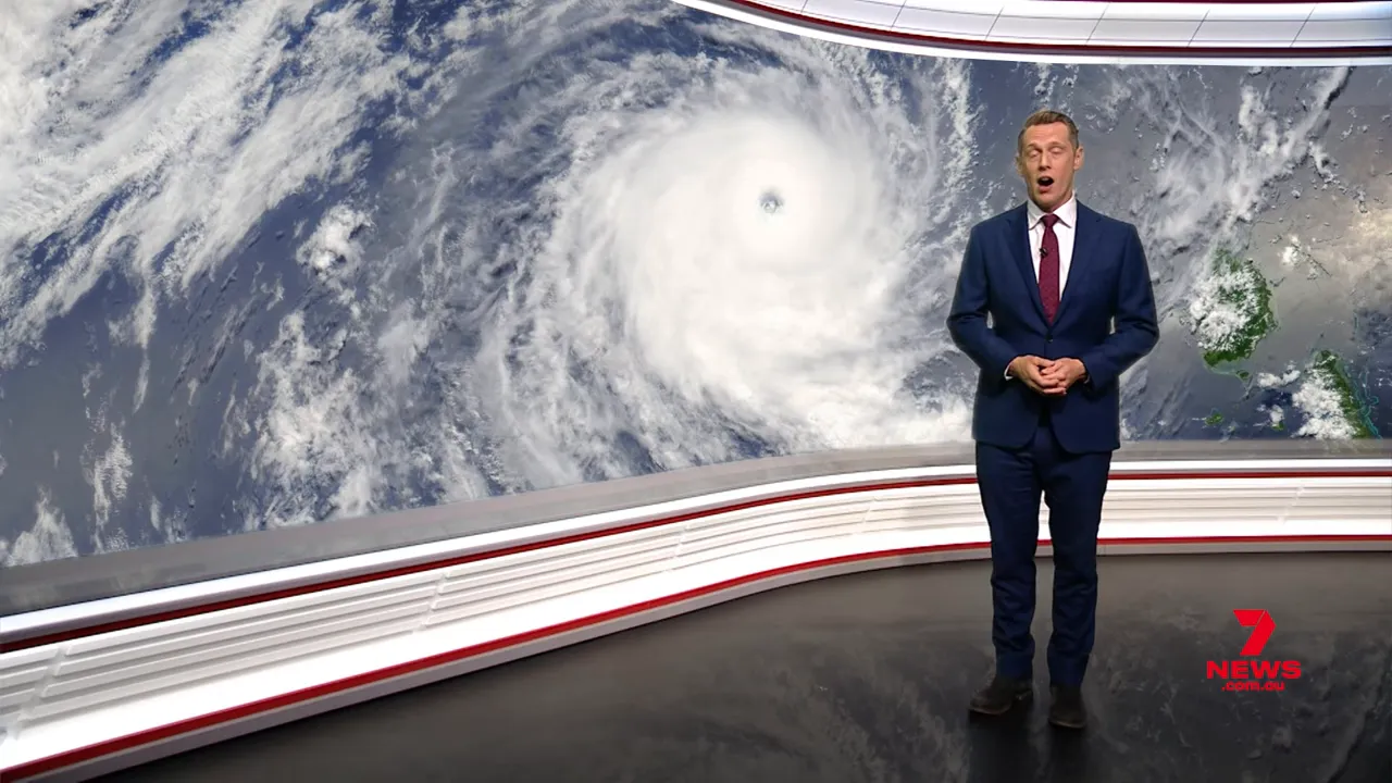Satellite image of a tropical cyclone with a clear eye and spiral cloud bands behind a news presenter